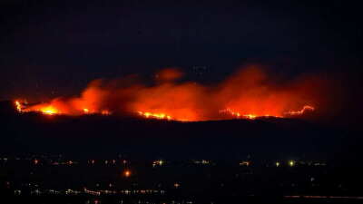 Línea de fuego sobre las montañas iluminando el cielo nocturno y luces de un poblado distante en la parte inferior. Línea de fuego sobre las montañas iluminando el cielo nocturno y luces de un poblado distante en la parte inferior.