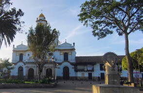 Iglesia católica de fachada blanca y cúpula amarilla frente al parque principal de Funza, Cundinamarca, con árboles alrededor.