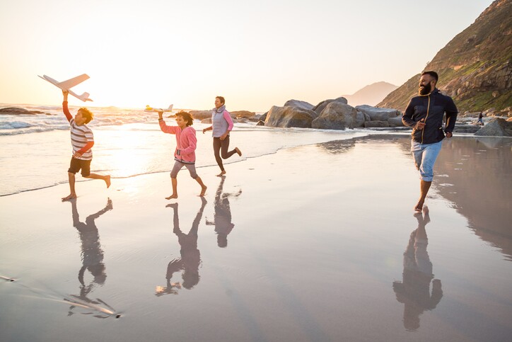 Mixed race family running along beach with toy planes