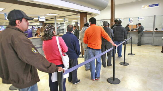 Personas haciendo fila en un banco mientras esperan ser atendidos.