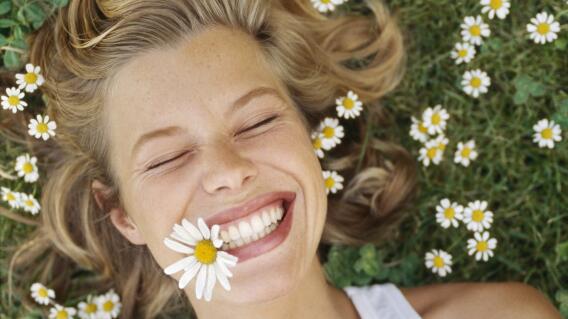 Young woman lying on grass, with daisy in mouth, smiling Young woman lying on grass, with daisy in mouth, smiling