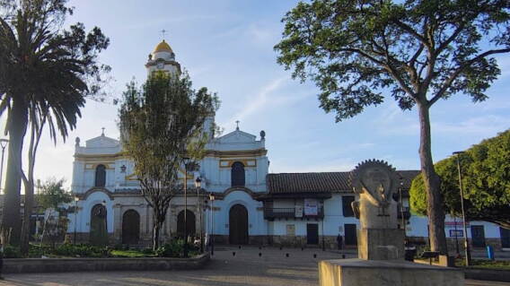 Iglesia católica de fachada blanca y cúpula amarilla frente al parque principal de Funza, Cundinamarca, con árboles alrededor.