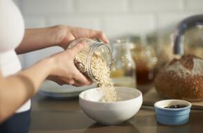 Woman pouring oats into bowl in kitchen, close up.