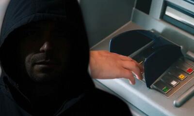 Hombre con capucha junto a un cajero automático. 