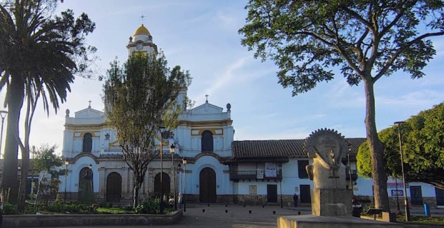 Iglesia católica de fachada blanca y cúpula amarilla frente al parque principal de Funza, Cundinamarca, con árboles alrededor.